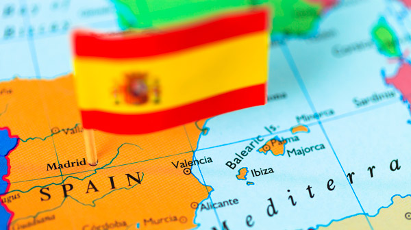 photo illustration of a map enlarged to focus on the country of Spain, with a small Spanish flag pin