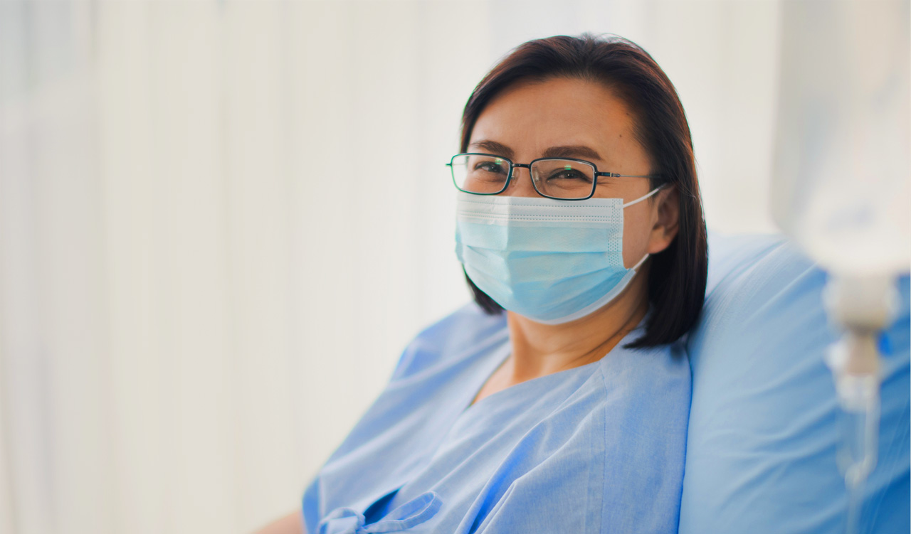 Asian woman smiling through mask, wearing hospital gown, getting ready for ECT procedure