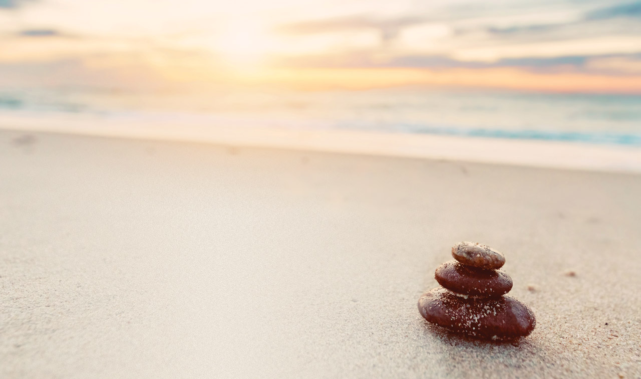 Photo illustration of a small cairn on a beach, during a sunrise