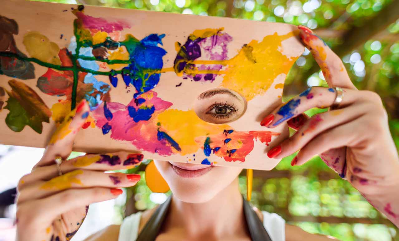 photo of woman's eye seeing through a hole in a colorful painting