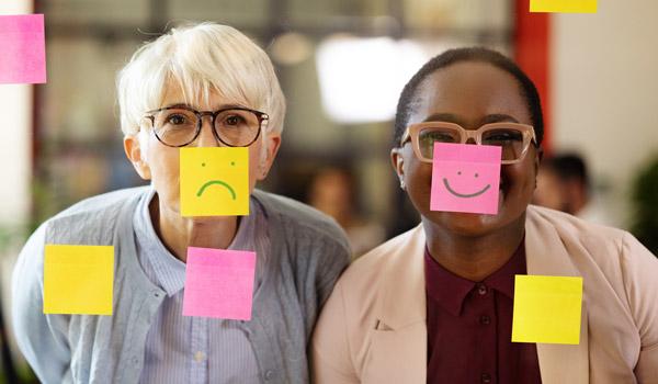 Photo of two women playfully with post-its on their faces with sad and happy smiles